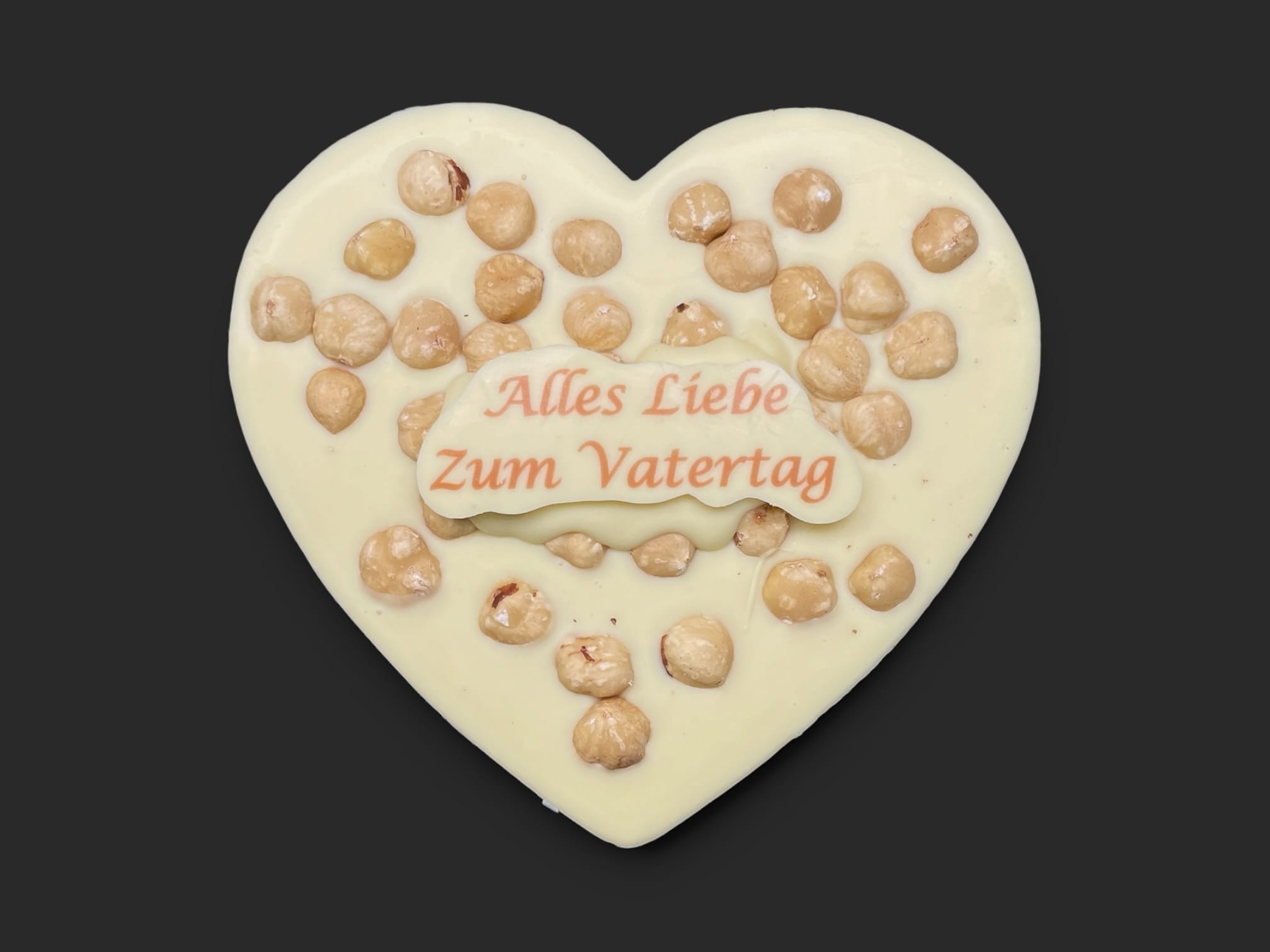 Schokoladenherz aus weißer Schokolade (36 % Kakao), mit Aufschrift „Schokoherz flach Vatertag Haselnüsse“