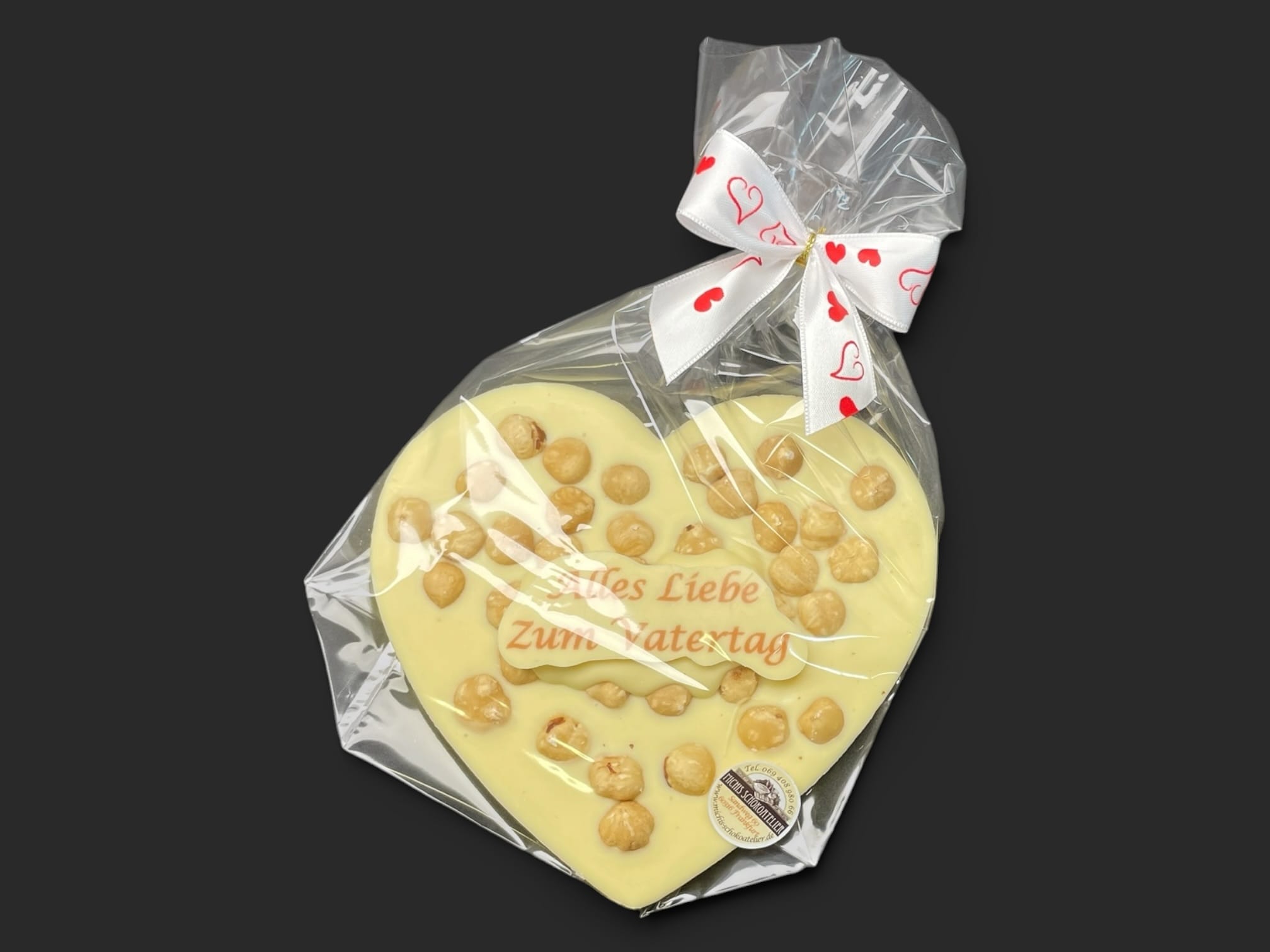 Schokoladenherz aus weißer Schokolade (36 % Kakao), mit Aufschrift „Schokoherz flach Vatertag Haselnüsse“, in Geschenkverpackung